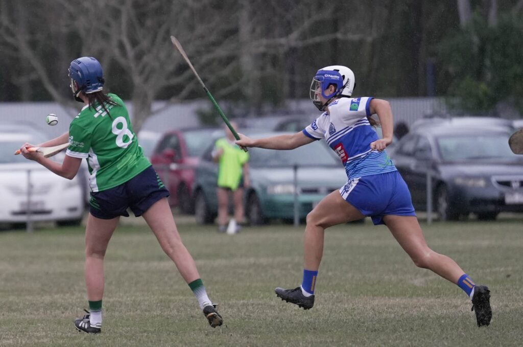 An Emeralds camogie player shoots for a score while under pressure from a Na Fianna player